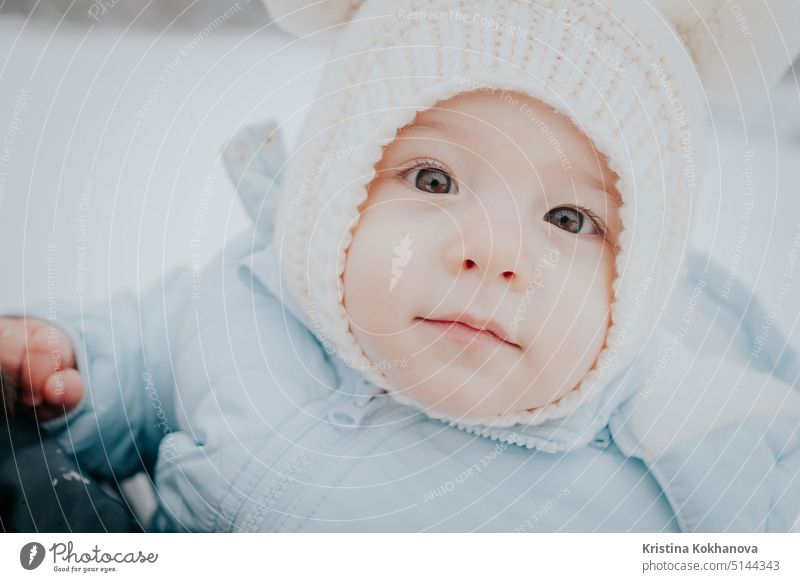 Cute portrait of little baby in winter hat with fluffy ears on snowy street background. family, son, toddler child concept. childhood cute adorable happy kid