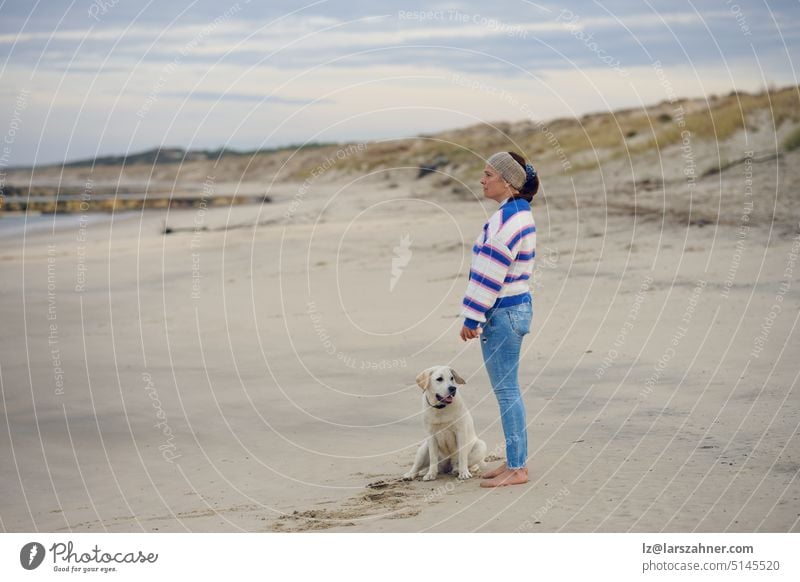Middle-aged brunette woman on the empty beach with her labrador retriever dog middle-aged winter profile copy space autumn surprised wet moist coast shore