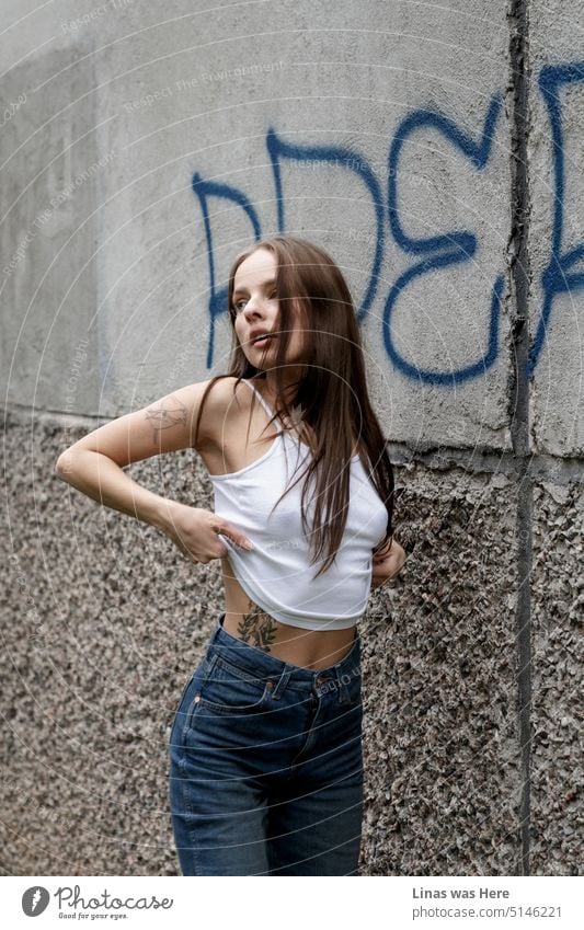 In this concrete jungle, a gorgeous brunette woman is in the action. Blue jeans and a white shirt. She’s in her casual fashion. A pretty inked girl is slowly undressing and showing her perfect sexy curves.
