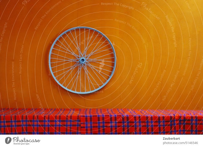 Rim of bicycle on orange wall in front of red checkered table cloth Wheel rim Bicycle Orange Red Checkered Massai Wall (building) Art Spokes Round Rotate