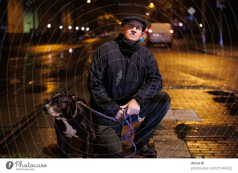 a friendly man with his dog in the rain at night on the street in the city, illuminated by a streetlight Man Dog Rain Street Town cars rail Background lights