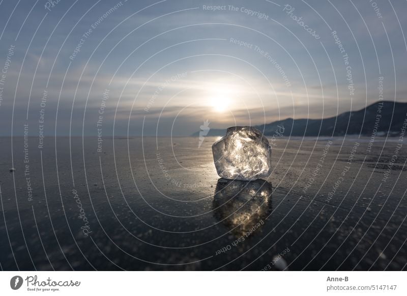 beautiful big glittering ice lump on a thick frozen lake in Siberia ( Baikal ) , in the background the slowly setting sun and a few hills. lump of ice