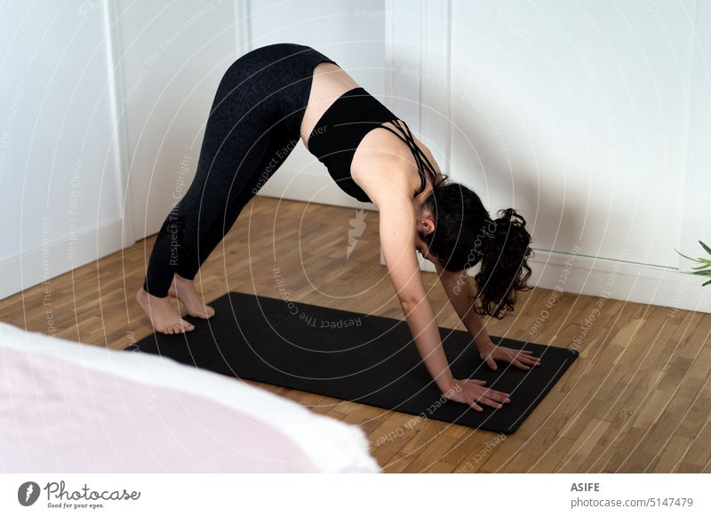 Young woman practising a yoga asana in her bedroom. exercise home young sport adho real people candid mukha svanasana downward pose mat floor position workout