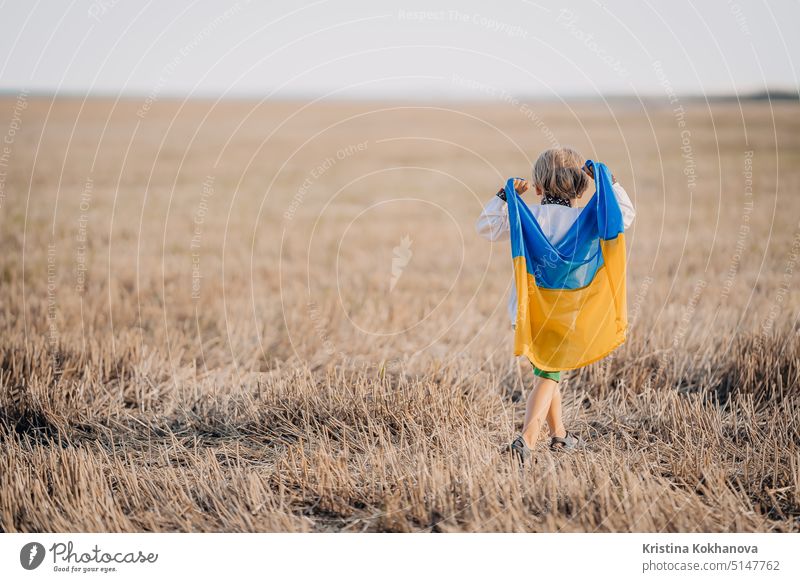 Happy little boy - Ukrainian patriot child with national flag in field after collection wheat, open area. Ukraine, peace, independence, freedom, win in war.