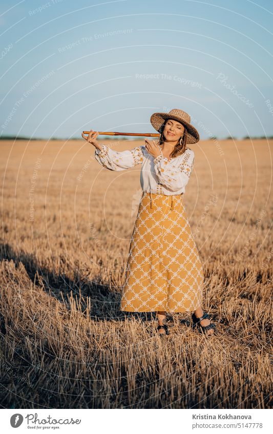 Rural woman plays on wooden flute - ukrainian telenka, tylynka in wheat field. Folk music, sopilka concept. Musical instrument. Musician in traditional embroidered shirt - Vyshyvanka.