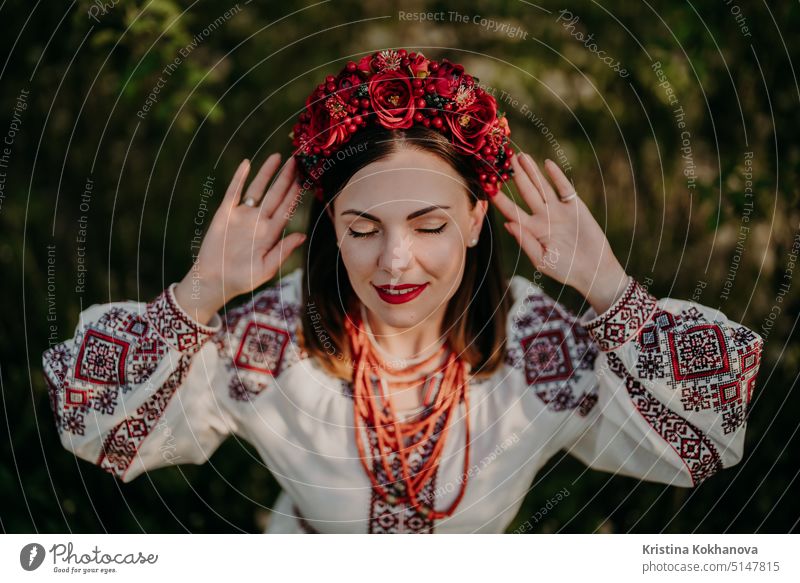 Attractive ukrainian woman in traditional embroidery vyshyvanka dress, ancient coral beads and red flowers wreath. Ukraine, freedom, culture, national costume, victory in war.