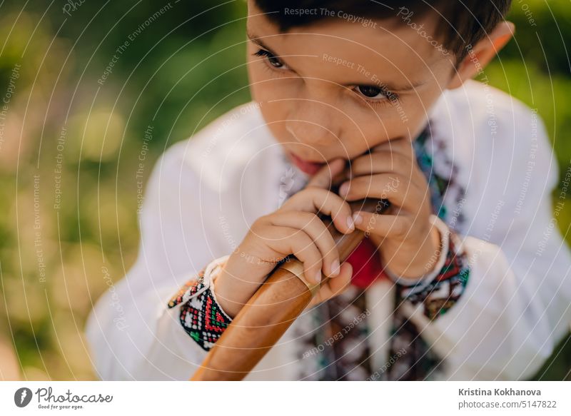 Portrait of little boy with woodwind wooden flute - ukrainian sopilka. Folk music concept. Musical instrument. Child in traditional embroidered shirt - Vyshyvanka.