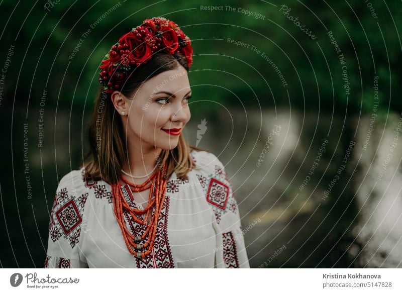 Pretty ukrainian woman in traditional embroidery vyshyvanka dress and red flowers wreath near river. Ukraine freedom, springtime, national costume, victory in war.