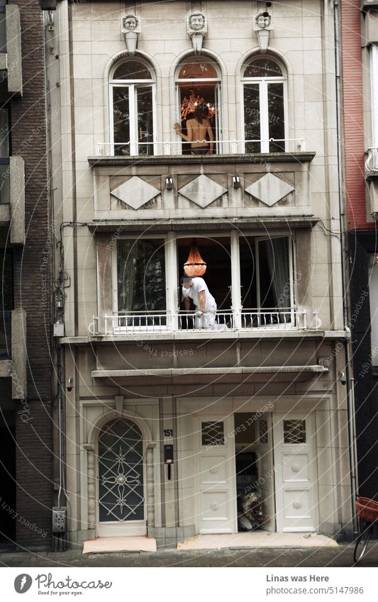 It’s a lively old town building. A topless woman on the third balcony. Two painters are working below. A cinematic shoot from the street of Antwerpen, Belgium.