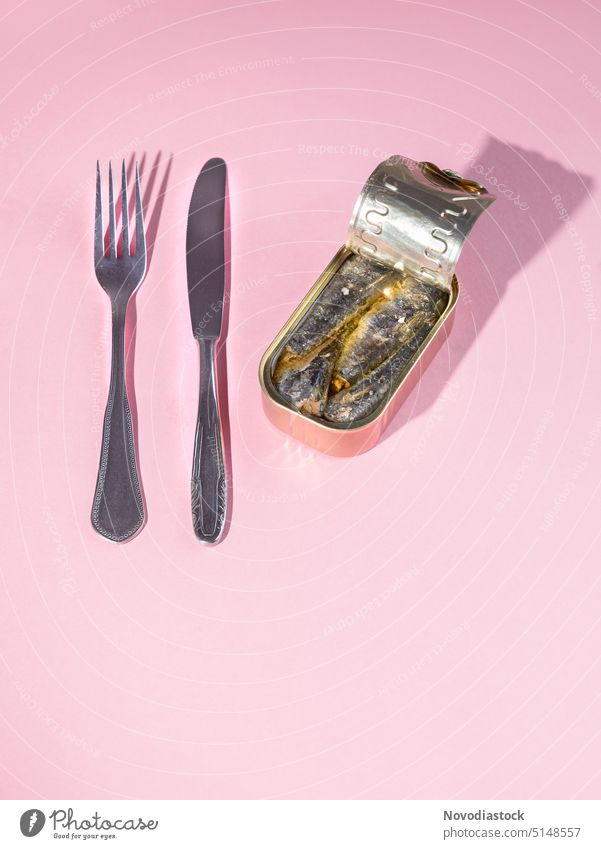 Sardines in a can, a knife and a fork, ready to be eaten, no plate, isolated on pink background Tin Tin of food canned food Canned fish sardines Fish preserved
