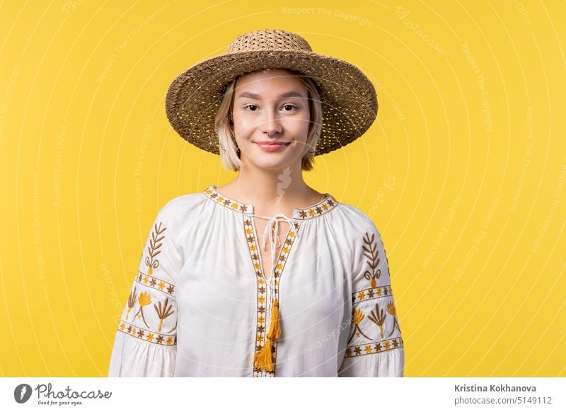 Portrait of young ukrainian blonde woman in traditional embroidered blouse on yellow studio background. Confident sunny outfit, straw hat. adult beautiful