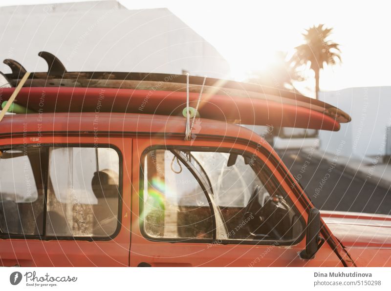 A stack of surfboards on a retro car roof with sun shining. Summer and surf background wallpaper. Vintage car roof with sandy surf boards stacked on it. Vacation mode. Easy relaxed lifestyle, living in the moment concept.