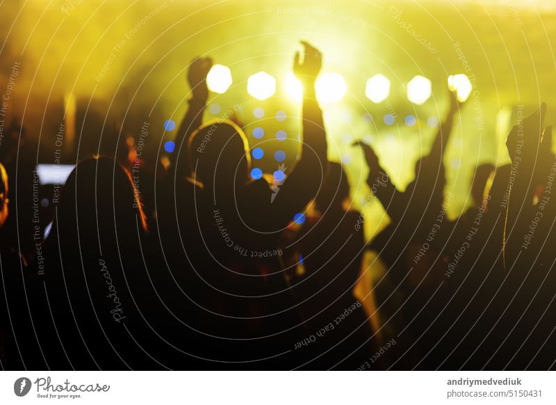 cheering crowd in front of bright yellow stage lights. Silhouette image of people dance in disco night club or concert at a music festival. applauding