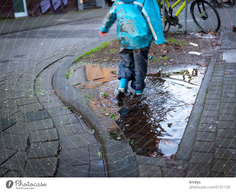 Child in mud clothes splashes in puddle Infancy Puddle Water Muding Rain gear Joy Wet Dirty Rubber boots Town Playing Mud clothes rainwear