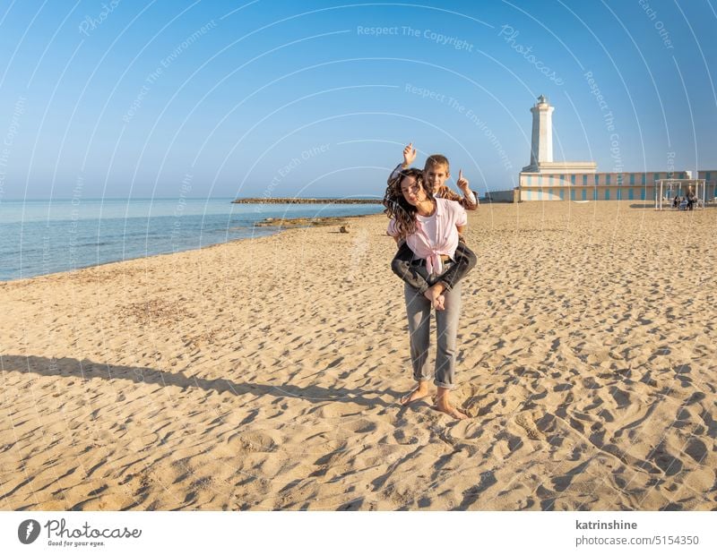 Happy Mother and son running on beach barefoot in a sunny day against the lighthouse sea sunset outdoor Toddler kid boy family together Mom fun smile sand