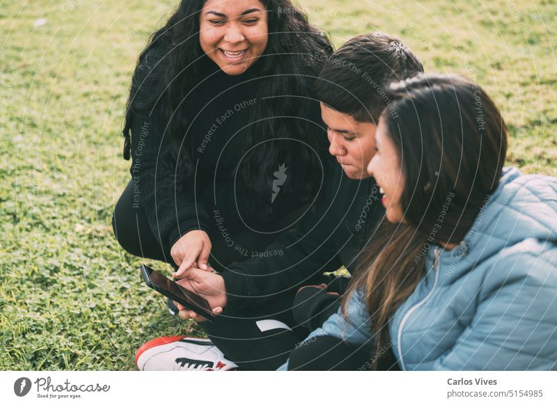 group of Latinos laughing sitting on the ground in a park with a smartphone accessibility argentina bag bonding broadcasting carefree connection copy space
