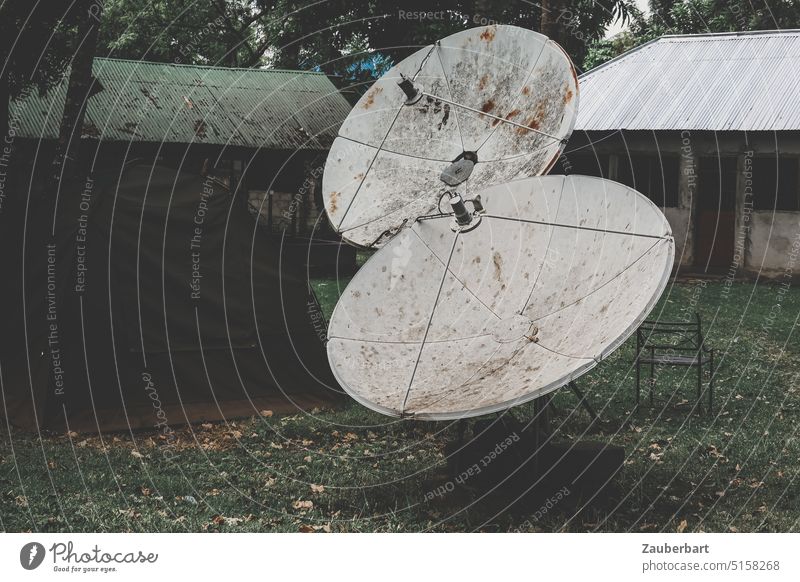 Antenna dishes stand next to tent and in front of houses covered with corrugated iron in gloomy atmosphere Receive Video Satellite satellite reception