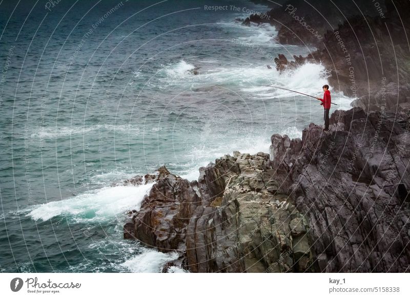 Boy with red sweater and fishing rod on rocky coast by sea Fishing (Angle) Fishing rod Boy (child) Young man somber Ocean Waves ocean Atlantic Ocean