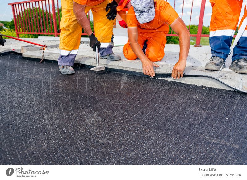 Workers apply black bitumen membrane strips for waterproofing roads and bridges to the curb of the sidewalk Apply Asphalt Attach Bitumen Bituminous Black Bridge