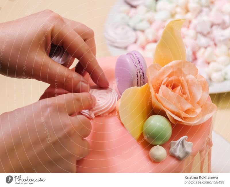 Unrecognisable woman decorating mousse glaze cake with rose, macarons, hands detail, focus on the cake. DIY, sequence, step by step, part of series. decoration