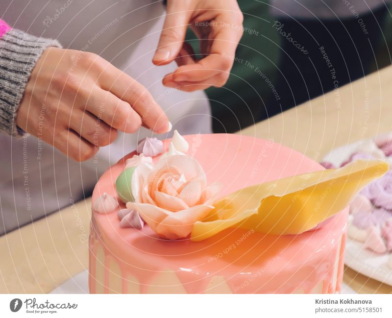 Unrecognisable woman decorating mousse glaze cake with rose, macarons, hands detail, focus on the cake. DIY, sequence, step by step, part of series. decoration