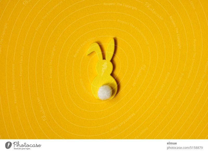 yellow stylized Easter bunny from behind with bent ear and white flower on yellow background / Easter Easter Bunny Hare & Rabbit & Bunny kink in the ear