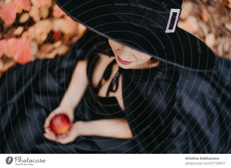 Portrait of woman as witch in black holding red apple as symbol of temptation anger art autumn background beautiful beauty bizarre celebration child contact