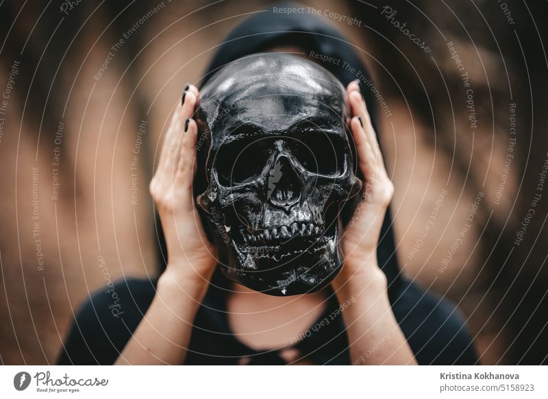 Witch woman in black clothes holds skull at level of head. Death Eater concept anatomical anatomy background bald biological biology body bone brain clipping