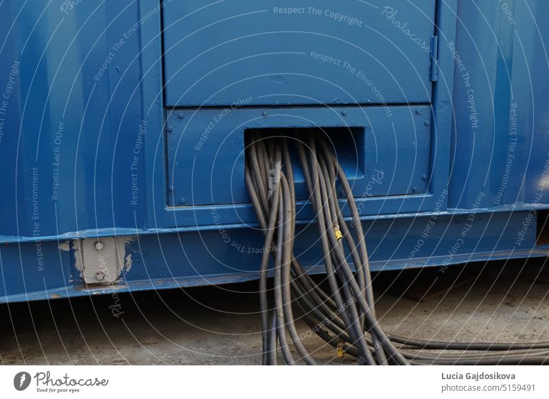 Close up view on bundle of black cables come out from blue power pack or portable generator for supply of electricity to the reefers on deck of loaded container vessel passing through ocean.