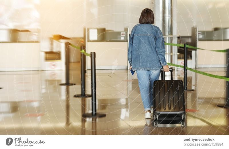 back view of middle aged woman traveling in casual clothes. Female in airport with suitcase going at the check-in desk while checking in for her flight. Passenger travel abroad on holiday or weekend