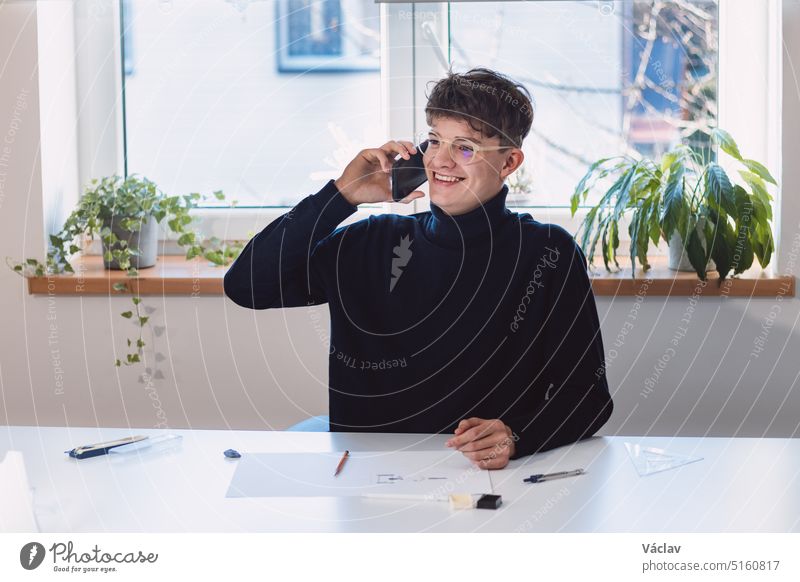Goal-oriented brown-haired businessman is on the phone with his supervisor and talks about his visions, at which he smiles. A young a ostentatious visionary in his office