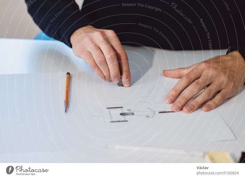 Close-up of a bright, businesslike, aspiring and young architect at his desk in his office. Drawing a new product on white paper. The work of a product designer