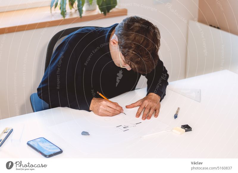 Brown-haired architect is thinking hard about how to create new product designs for a new futuristic world. He works with his own creativity. Compass, pencil, ruler and paper. Creative home office