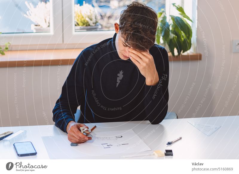 Entrepreneur and architect is thinking hard about a new design for a new prototype, which he draws in pencil on paper. Inventing a new design. An ambitious young boy. Illuminated workroom