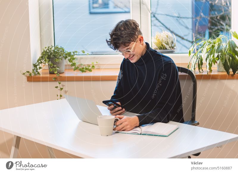 Purposeful brown-haired entrepreneur with a smile on his face answers his clients on his mobile phone in his office with ample daylight. Working from home