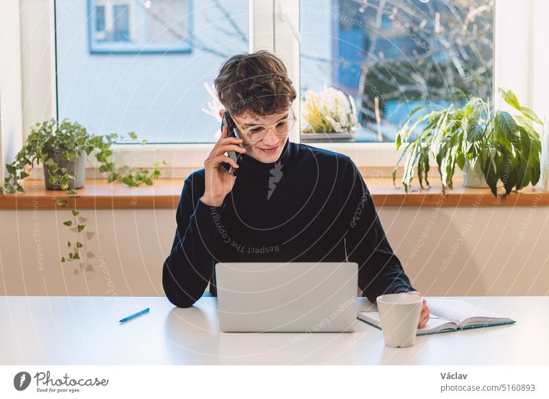 Purposeful brown-haired businessman is on the phone with an exiting client, jotting notes in his diary. Online business meeting with client. Young visionary