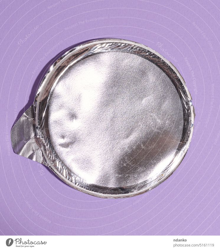 Aluminum round lid from under the package with chips on a purple background, flat lay aluminium gray grey industrial kitchen nobody sheet shiny silver studio