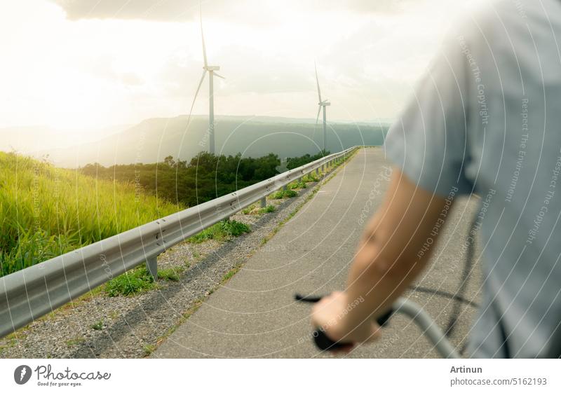 Selective focus on wind farm with rearview of person riding a bicycle as foreground. Wind energy. Wind power. Sustainable, renewable energy. Wind turbines generate electricity. Sustainable lifestyle.