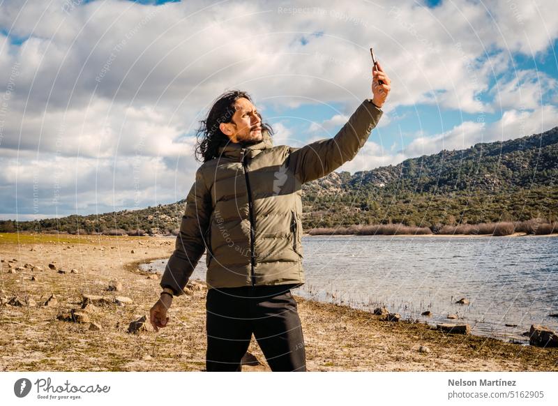 A man with long hair taking a selfie on the shore of a lake landscape winter mountain person slate beauty nature epic tree driftwood river morning architecture