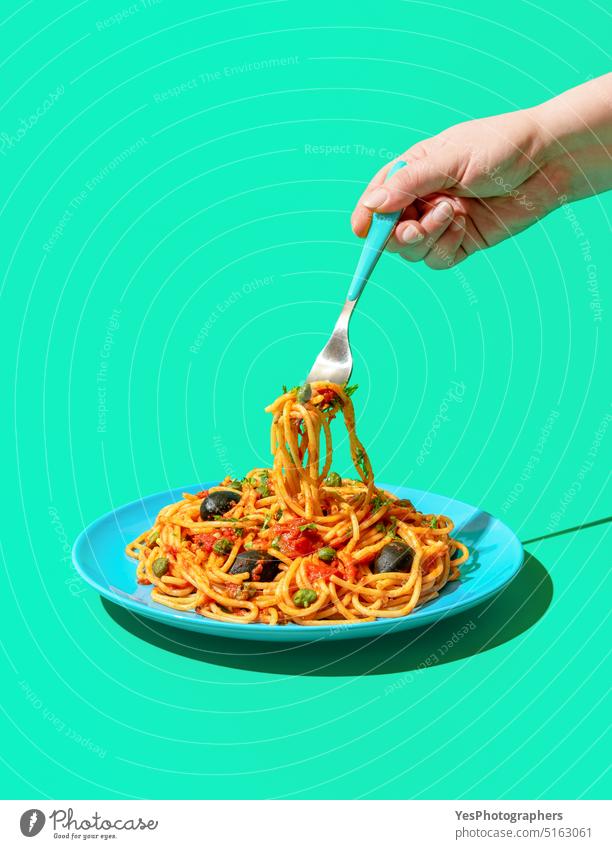 Eating spaghetti puttanesca, a vegan pasta dish, minimalist on a green background blue bright capers carbs close-up color cooked copy space cuisine cut out