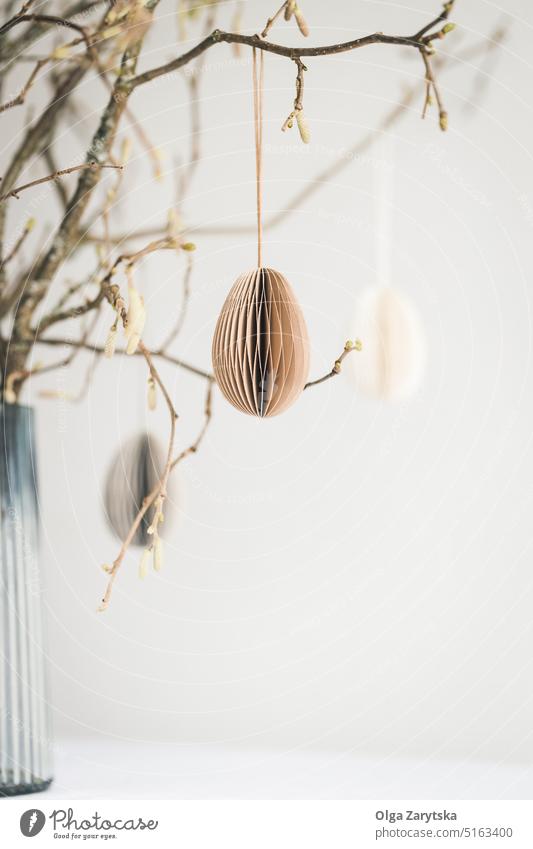 Easter eggs hanging on branches against white wall. easter paper decoration table vase tablescape egg-shaped pastel ornaments scandinavian style lifestyle DIY