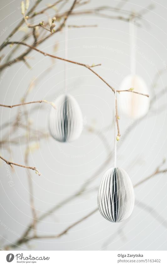 Easter paper eggs hanging on branches. easter decoration egg-shaped pastel ornaments scandinavian style lifestyle twig DIY craft idea beautiful simple cardboard