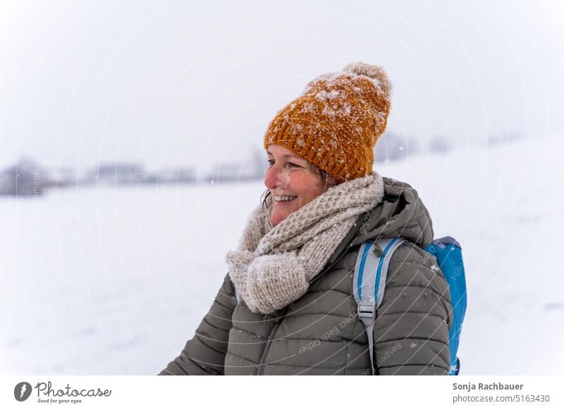 A smiling woman with cap and scarf in snow Woman Smiling Cap Snow Winter Scarf Cold Face 50 plus Feminine natural beauty portrait 1 Exterior shot Hiking