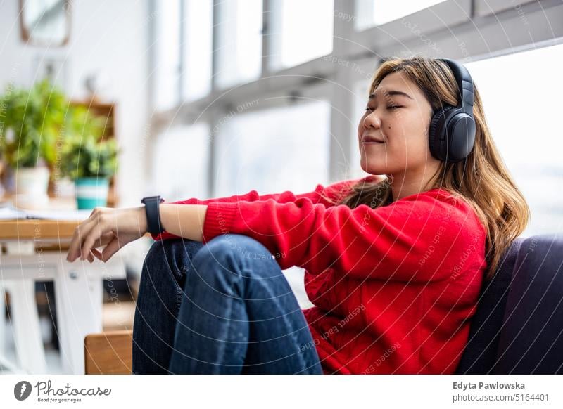 Young woman using headphones while relaxing on the sofa real people millennials student indoors loft window natural girl adult attractive successful confident