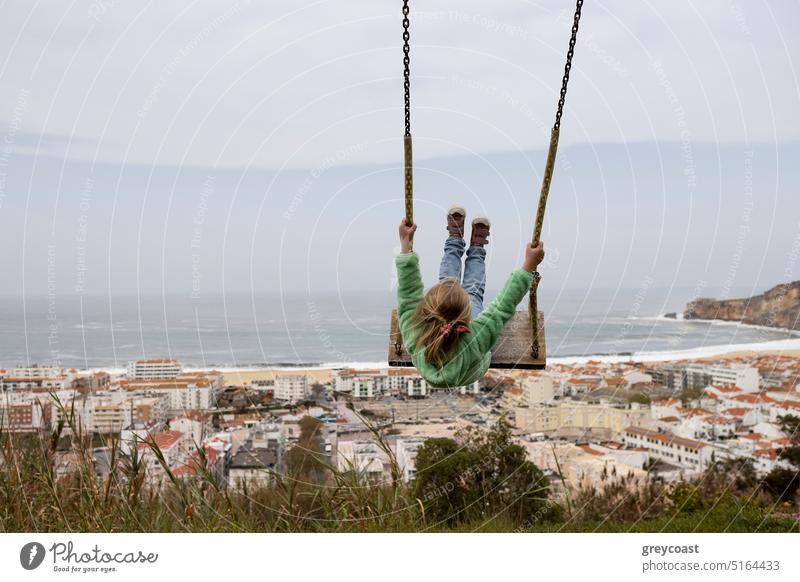 Little girl swinging against the scene of Nazare coast in Portugal child sea kid fun look happy ocean happiness playground childhood outdoor joy little vacation