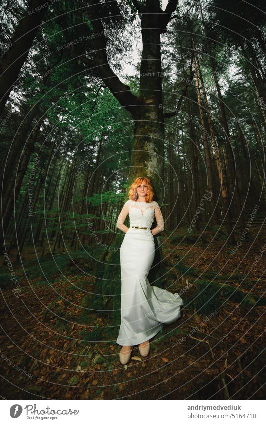 beautiful young red-haired bride in the forest. woman in long white dress outdoors on summer day. wedding day woods bouquet stylish background wreath nature