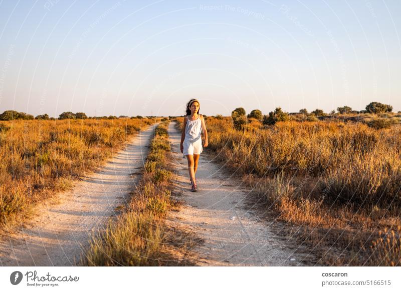 Lonely girl walking on a country road at sunset. beautiful beauty blue sky caucasian child childhood children countryside day farmer female field forest freedom
