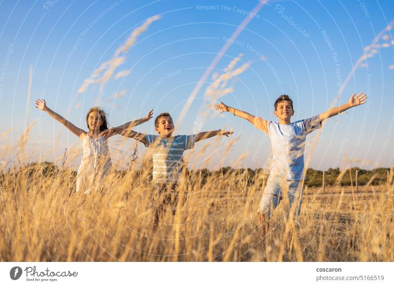 Three kids with open arms in the countryside at summer air background beautiful child childhood concept day dry enjoy family field free freedom friends fun girl