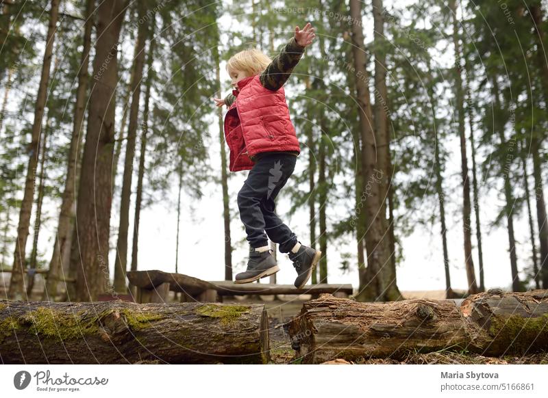 Little boy in red vest is playing branch and having fun in forest on early spring day. Activity for children. Outdoor recreation for family nature activity log