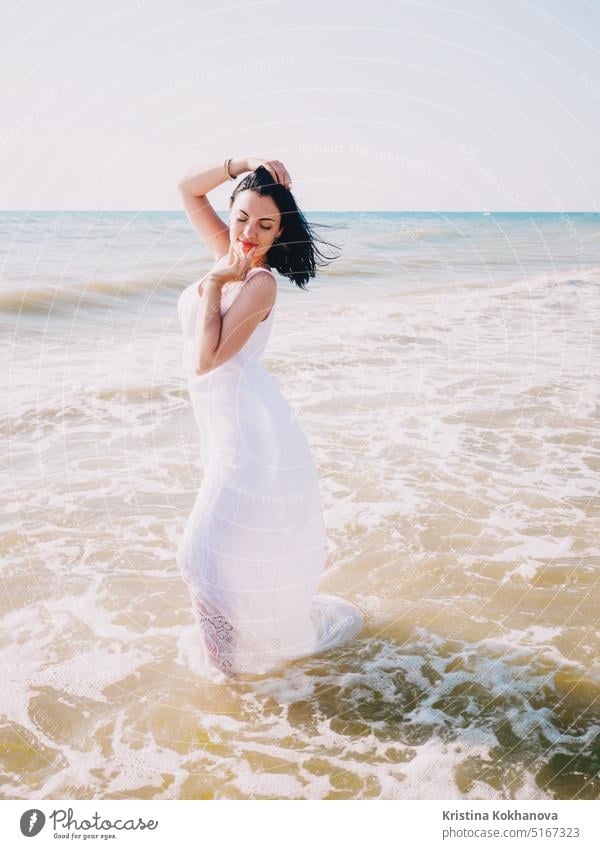 Gypsy young woman in white maxi long dress standing on waves in sea beach water sand summer walking women caucasian female freedom nature outdoors travel